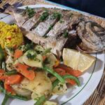 A plate with an entire fried fish on it, alongside vegetables and yellow rice