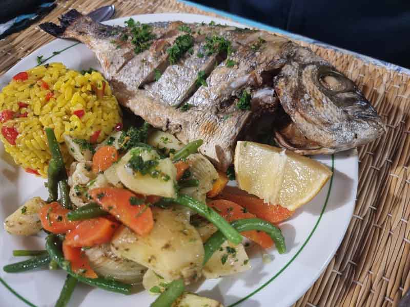 A plate with an entire fried fish on it, alongside vegetables and yellow rice
