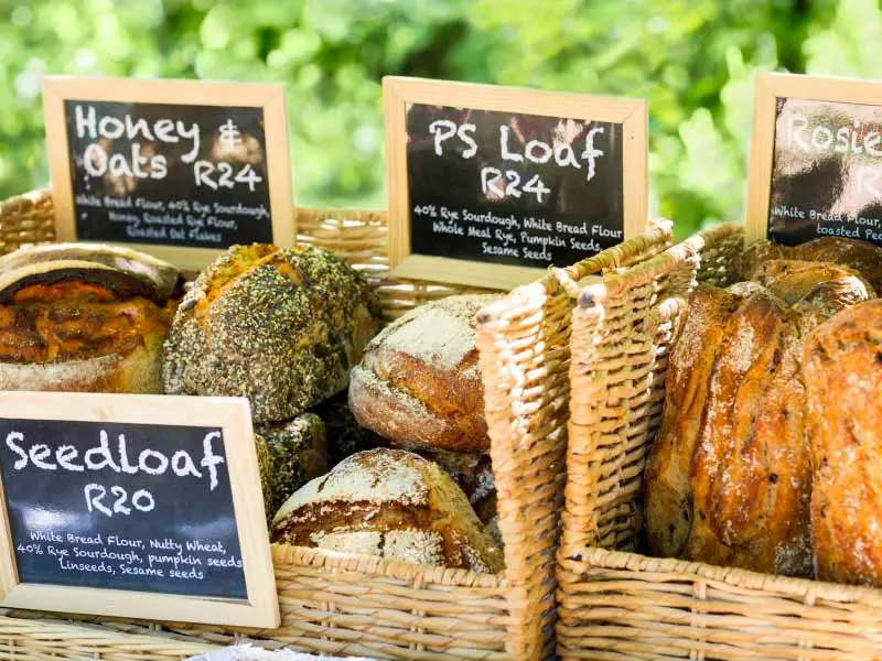 a close-up of crates with different artisanal loaf of breads, with black board which show the prices for each in South African Rands.