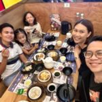 A group of people gathered around a table with a lot of small dishes on it, smiling at the camera.