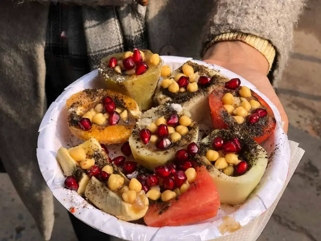 A platter with hollowed fruits filled with chickpeas and pomegranate seeds, topped with masala.