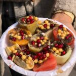 A platter with hollowed fruits filled with chickpeas and pomegranate seeds, topped with masala.