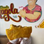 a close-up of a hand holding an arepa de huevo. Half of it is eaten. The arepa has a golden brown colour and is filled with ground meat