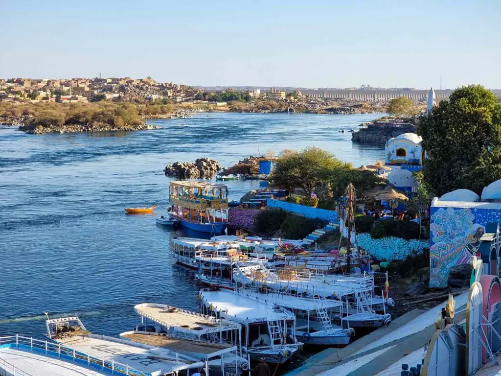 A view of the dock in the Nubian village in Aswan. There are boats anchored just in front of a staircase leading to the village. Behind, there is the water of the Nile River.