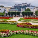 The castle on the hill in Salzburg, seen from the Mirabel gardens. The lawns are landscaped with red and yellow flowers.