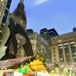 The Picasso Statue in Daley Plaza, Chicago. You can see the tall buildings in the back, and the rooftops of the Christmas huts at the bottom. it is dark outside and the fairy lights are on.