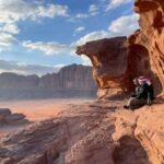 Hiking in Jordan: A Comprehensive Guide Two men sitting on the edge of the rock. They are wearing black clothes and puffer jackets, and have turbans on their heads.
