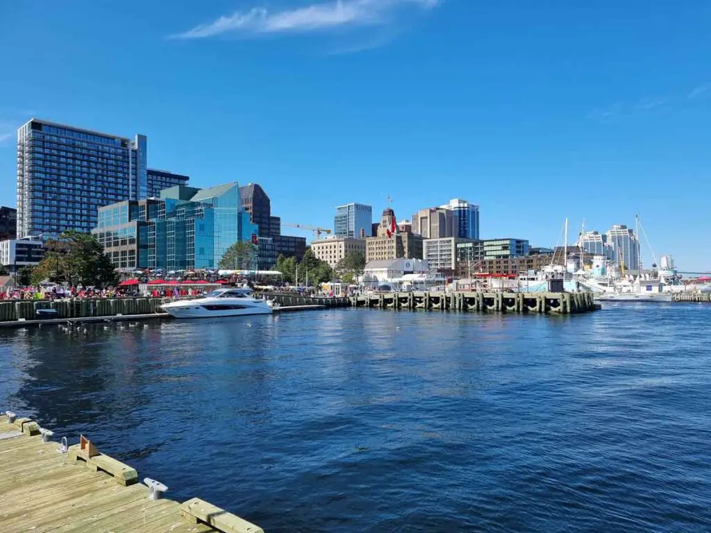 The waterfront in Halifax, seen from one of the piers. There is a mix of modern and old buildings, as well as small boats anchored by the wooden piers. The sky is blue, without any clouds.