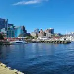 The waterfront in Halifax, seen from one of the piers. There is a mix of modern and old buildings, as well as small boats anchored by the wooden piers. The sky is blue, without any clouds.