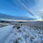 A wintery landscape, with snow on the ground and three wind turbines in the background.