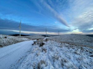 A wintery landscape, with snow on the ground and three wind turbines in the background.