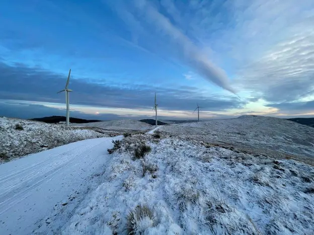A wintery landscape, with snow on the ground and three wind turbines in the background.