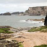 A remove beach in Northern Ireland, surrounded by very high cliffs. There is a group of people on a small hill, on the left of the photo.