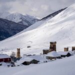 A small village at the foothills of a mountain slope, covered in snow.