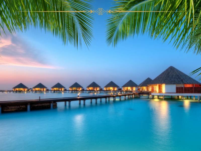 A sunset photo over the over the water bungalows in the Maldives. The lights are on in each of the bungalows.