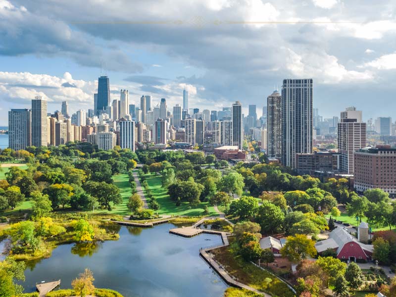 An aerial photo of Chicago on a cloudy day. In the background you can see tall sky scrapers. In the foreground there is a large park with a lake in the middle.