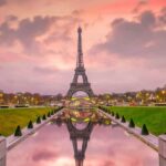Do You Know It's Illegal To Share Photos Of The Eiffel Tower By Night? Eiffel Tower with a fountain of water in front of it, in which it reflects and a pink sky. The photo has been taken at sunrise and there are no people around.