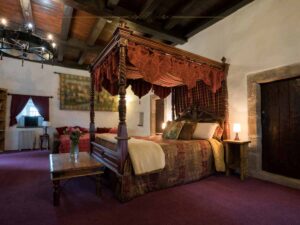 A medieval room inside a castle, with a four poster bed with a canopy on the top.