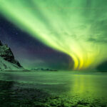 a green and yellow aurora borealis over a body of water in Iceland