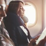 Two women sitting next to each other on a plane. One is sleeping, the other one is reading. The image has a sepia tone with a lot of brown tones.
