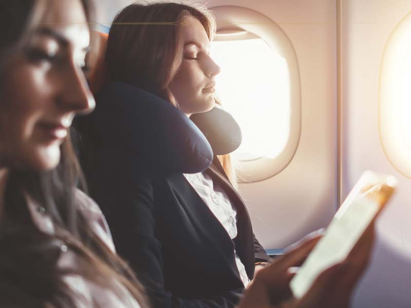 Two women sitting next to each other on a plane. One is sleeping, the other one is reading. The image has a sepia tone with a lot of brown tones.