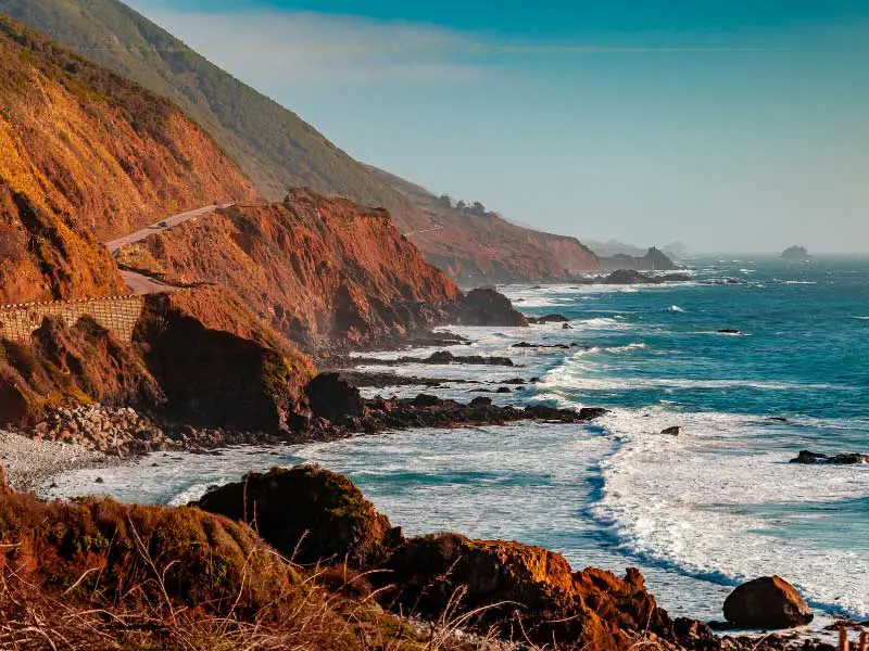 A road crossing cliffs next to the ocean. The waves crashing into the rocks are huge.