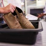 An airport tray with a pair of brown men shoe's just getting placed in it.