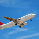 The Hottest New Flight Routes Taking Off This September A plane with a red tail flying over a blue sky.