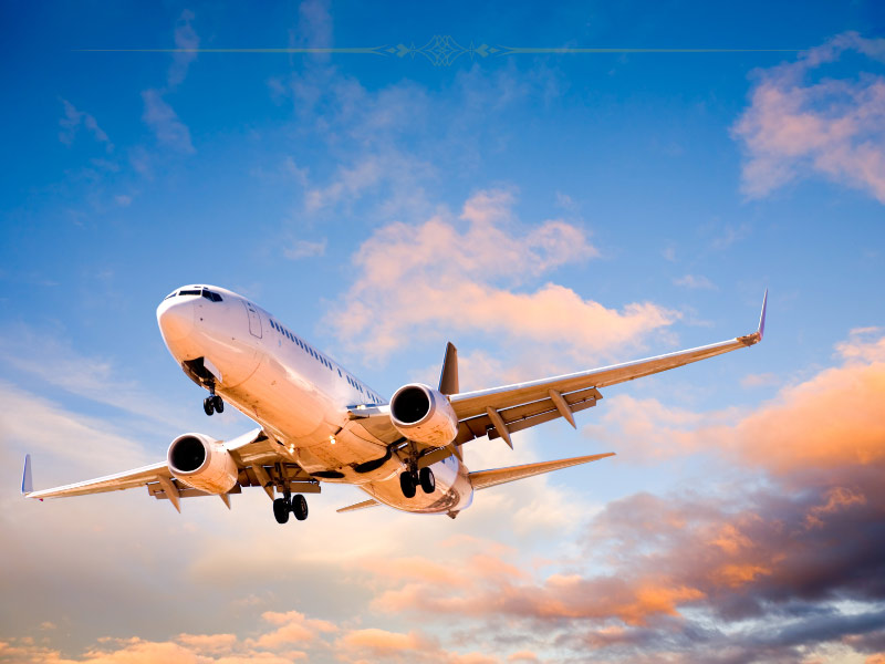 A white plane flying at sunset. The clouds behind are pink.