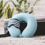 A light blue travel pillow leaning against a black suitcase