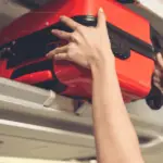 A close-up of an orange hand luggage being put in the overhead compartment on a plane.