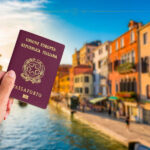 A hand holding an Italian passport against a background of a canal in Venice.