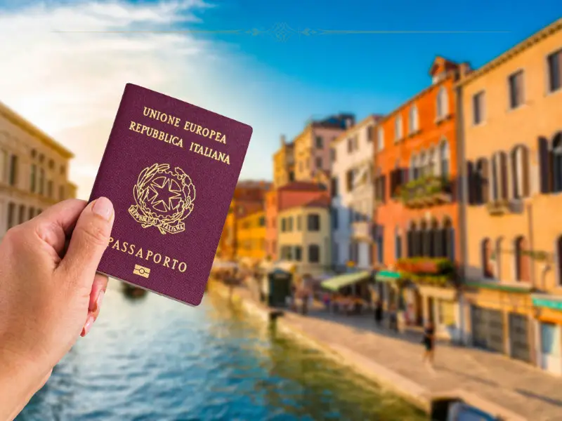 A hand holding an Italian passport against a background of a canal in Venice.