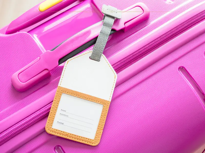 A pink suitcase with a luggage tag attached to the top.