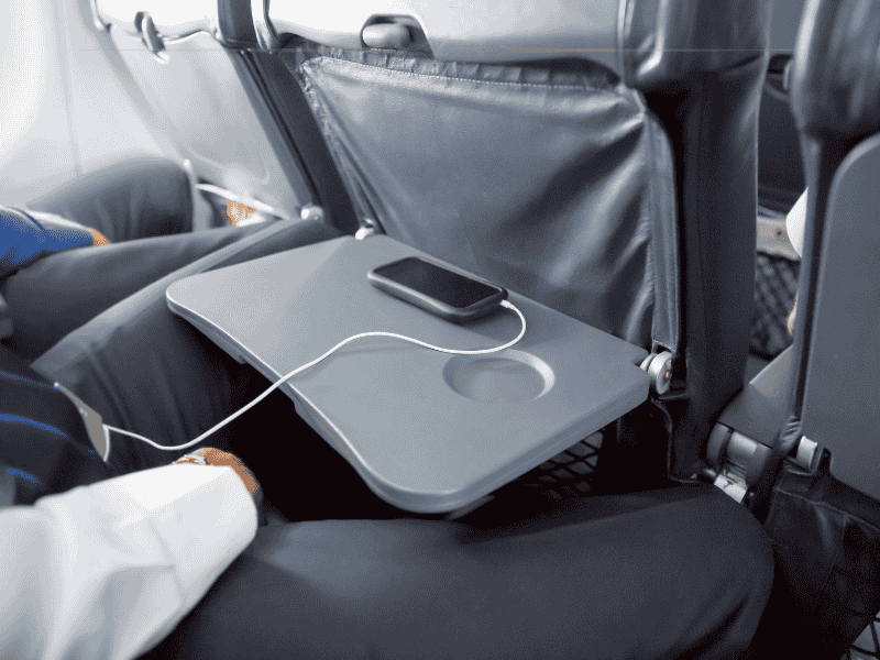 A close-up of a man sitting in the middle seat, with the tray down and a phone on the tray.