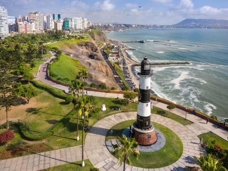 An aerial photo of a lighthouse on top of the cliffs. The ocean is on the right hand side.