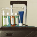 A see-through bag with liquid containers in it, on top of a carry-on bag.