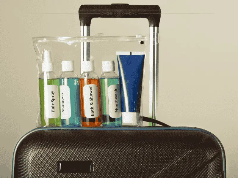 A see-through bag with liquid containers in it, on top of a carry-on bag.