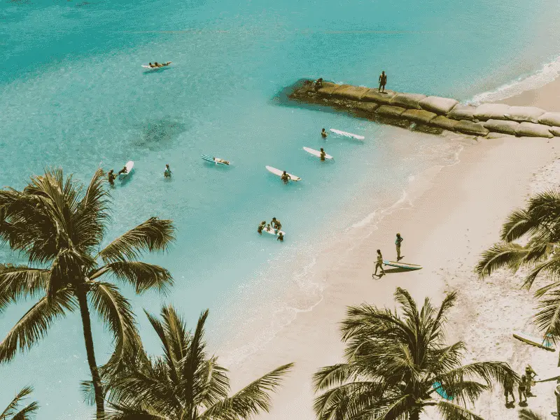 A tropical beach photographed from above, by a drone.There are people in the water, with their surf boards.