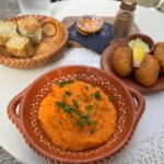 A ceramic plate with an orange mash in it. Next to it there is another plate with three meat balls next to an orange sauce. Behind there is a bowl with bread.