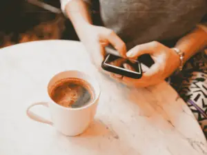 A close-up of a woman texting in a cafe, with a cup of coffee on the table next to her.