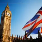 A photo of Big Ben on a sunny day, with a UK flag on the right hand side of the photo.