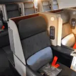 A photo of a first class section on a plane, with flat chairs and cushions on them