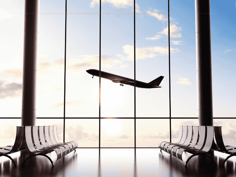 A plane seen taking off from the large windows of an airport.