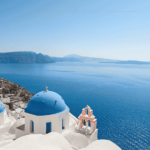 White buildings with blue domes as rooftops, overlooking the blue sea. There is no cloud on the blue sky