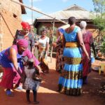 A group of women dressed in colourful clothes, dancing in a garden in a village in Tanzania
