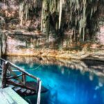The entrance to a cenote, with a wooden board on the left and the azure coloured water on the right.