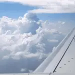 The wing of a plane passing through fluffy clouds
