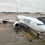 A white plane with Westjet written on it at the gate, at Gatwick airport, on a rainy day.
