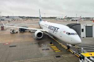 A white plane with Westjet written on it at the gate, at Gatwick airport, on a rainy day.